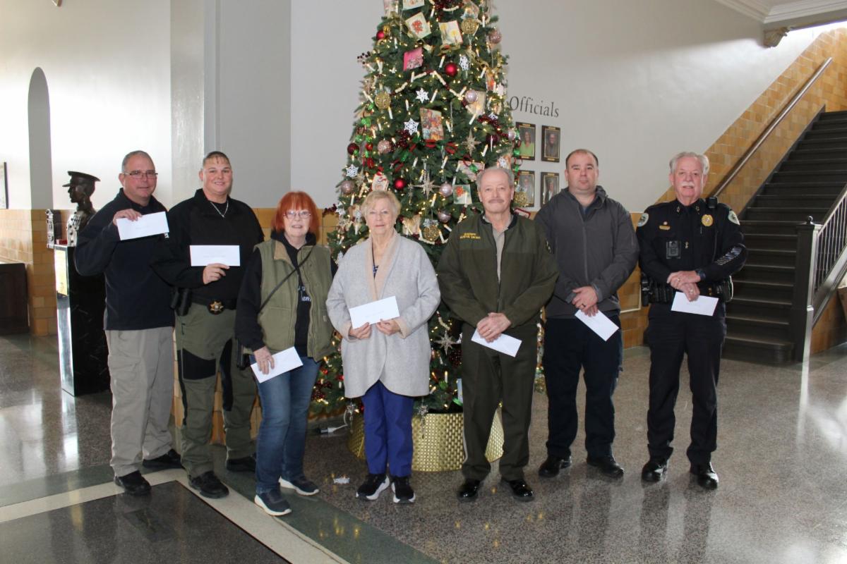 Donation recipients, as listed in the story, holding check envelopes and standing in front of the Courthouse indoor Christmas tree.