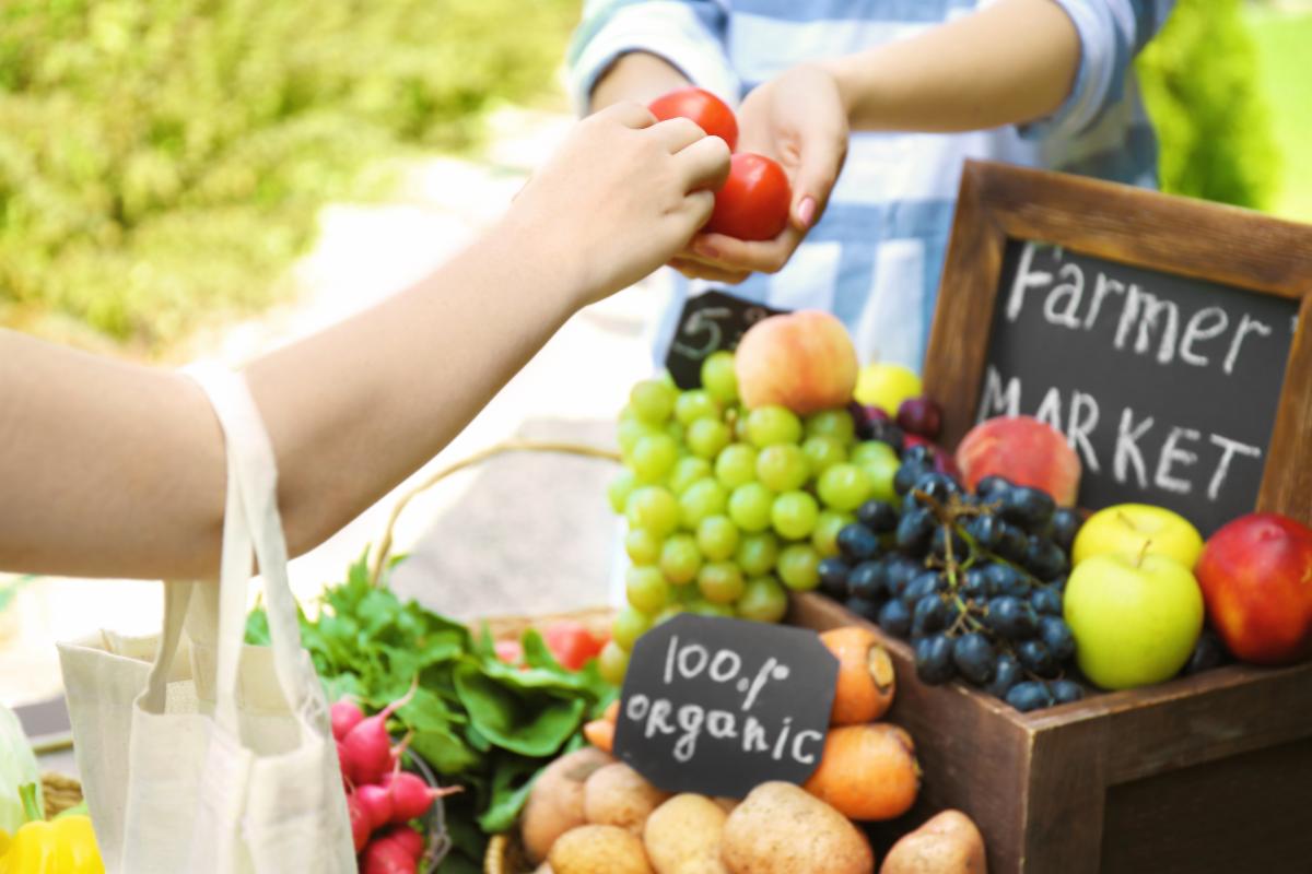 Customer receives tomatoes at a farmer's market beside a display of fresh produce.â