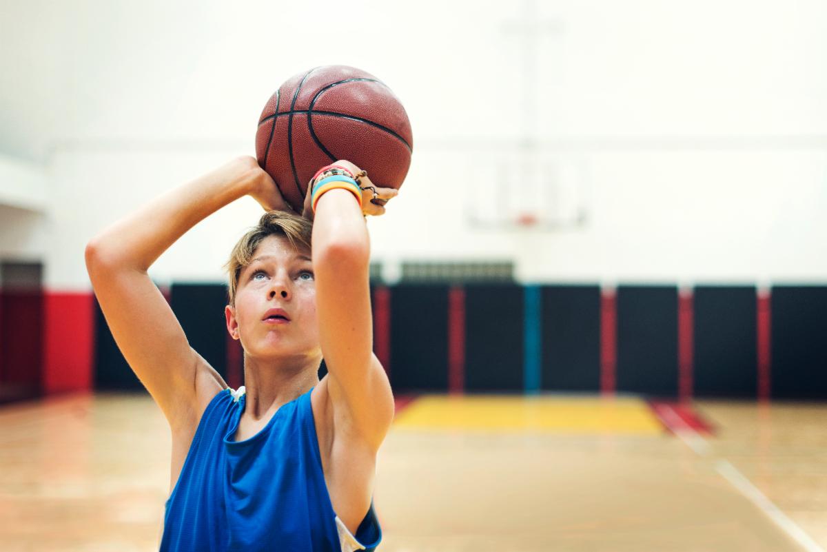 Young basketball player in a blue jersey prepares to shoot a basketball inside a gymnasium.