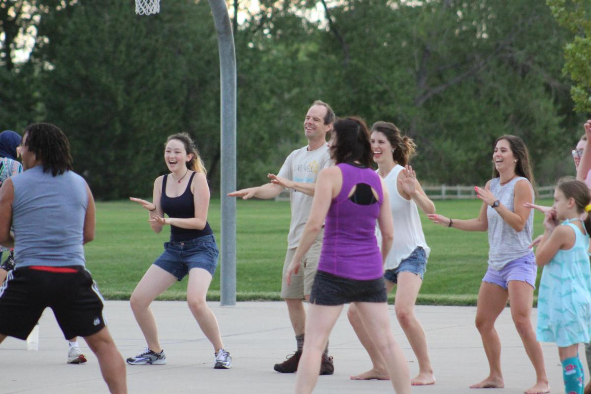 Adults and children participate in an outdoor fitness class on a paved court.