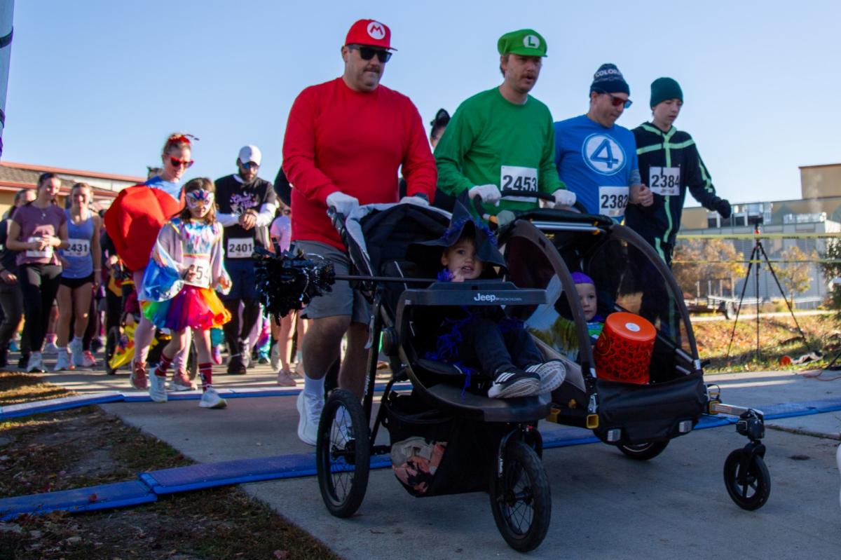 Costumed participants and families with children in strollers take part in an outdoor fun run.