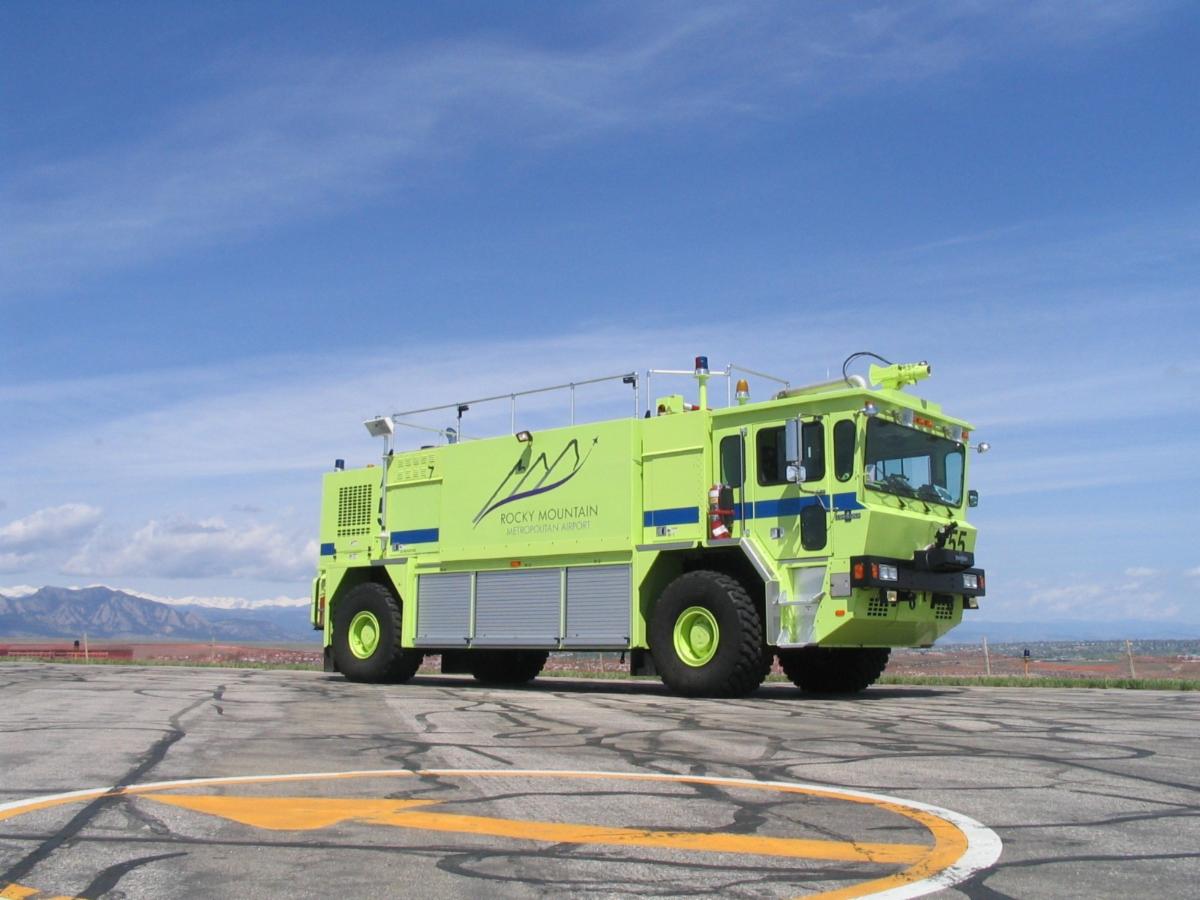 Bright green Rocky Mountain Metropolitan Airport fire and rescue truck parked on an airport tarmac with the Rocky Mountains in the background.