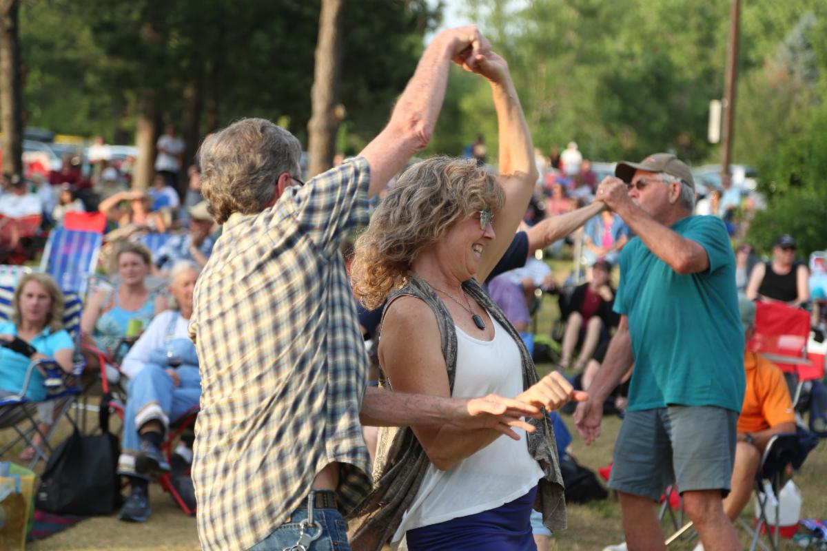 Couples dance in front of a seated crowd during an outdoor performance in a park.