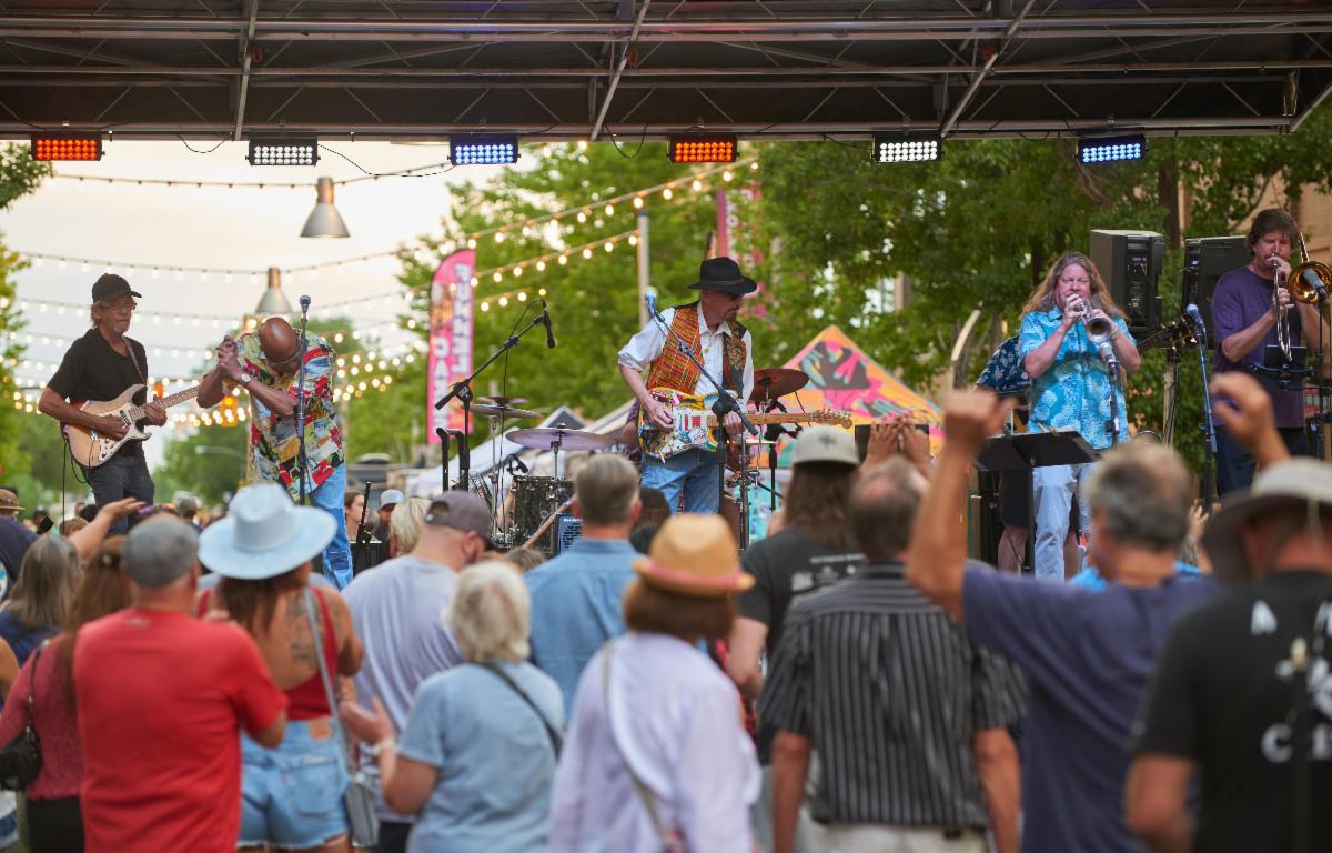 Band performs on an outdoor stage for a crowd at a summer event.