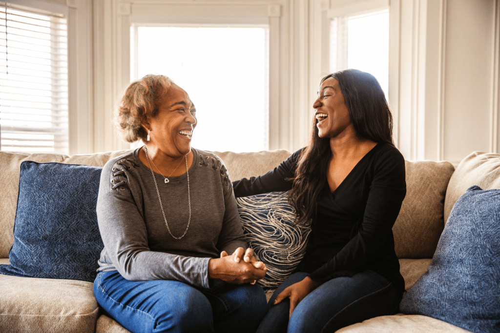 Two women sit on a couch, laughing together.