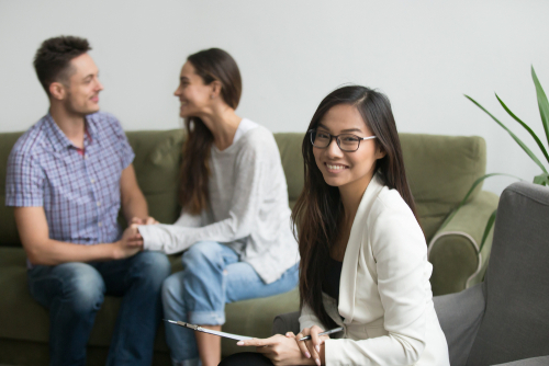 Portrait of smiling female asian counselor with happy couple at background_ professional chinese psychologist looking at camera_ marriage counseling therapy and family problems solution concept
