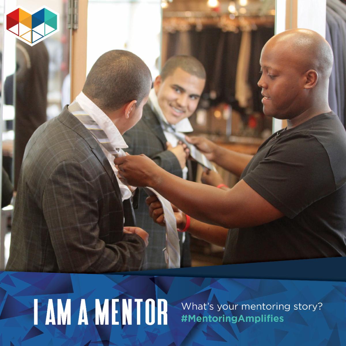 A man fastens a tie for another man who is looking in a mirror. Below reads: I am a mentor. What's your mentoring story? #MentoringAmplifies