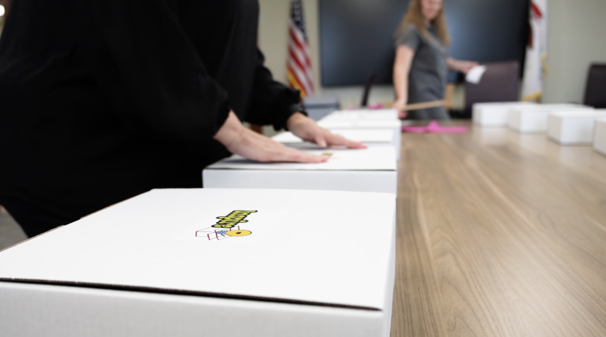 Adults preparing and packing row of boxes on table. Each box has logo for Inspire