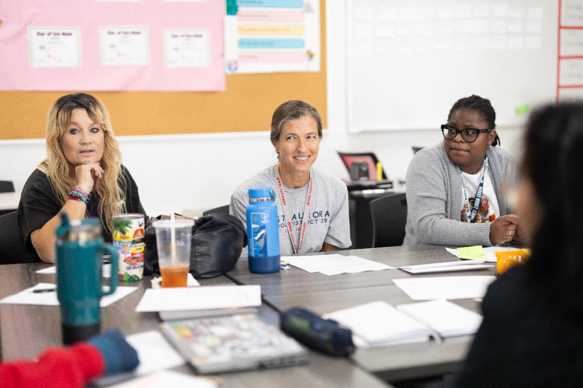 Three adults sitting at a table together in a classroom.