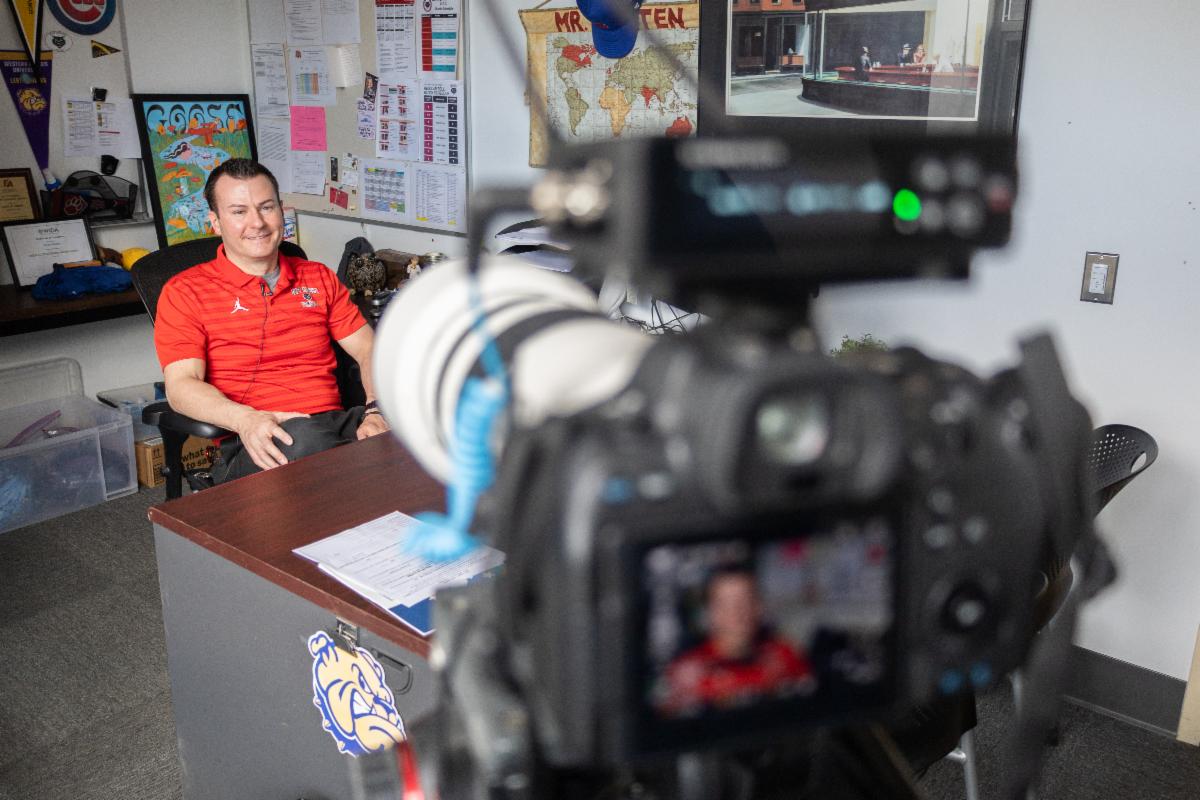 a close up of a camera taking a photo of an individual sitting at a desk.