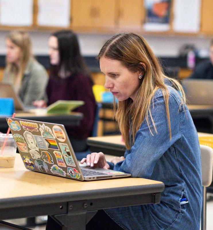 Adult sitting at a table browsing through a laptop.