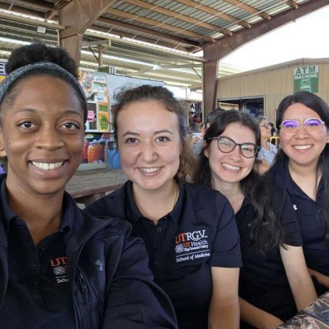 Four female medical students smiling. All are wearing black shirts with a collar; there a logo on the right hand side of the UTRGV School of Medicine.