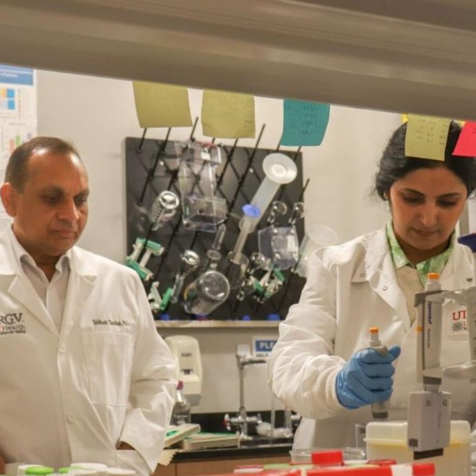 Two scientists in lab coats work in a university laboratory. One is focused on an experiment, holding a pipette. The setting is organized and professional.