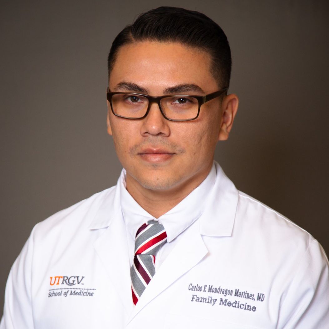 Man in a white coat with glasses, wearing a striped tie. The coat displays "UTRGV School of Medicine" and "Family Medicine." Professional appearance.