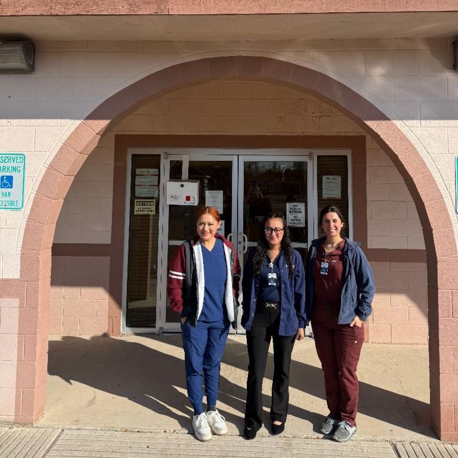 Three healthcare professionals in scrubs stand smiling outside the La Victoria Community Center, beneath the UTHealth Rio Grande Valley sign, conveying community support.