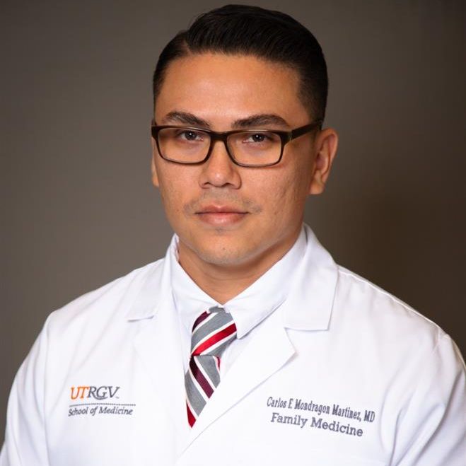 Man in a white lab coat and striped tie, wearing glasses, poses against a neutral background. "School of Medicine" is embroidered on the coat. Professional tone.