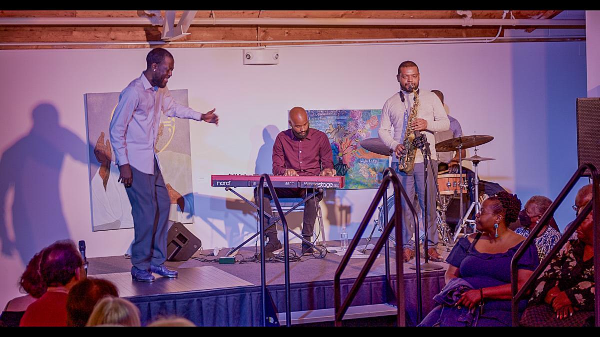Image capturing Baakari Wilder showcasing his tap dancing skills on stage alongside two other musicians.