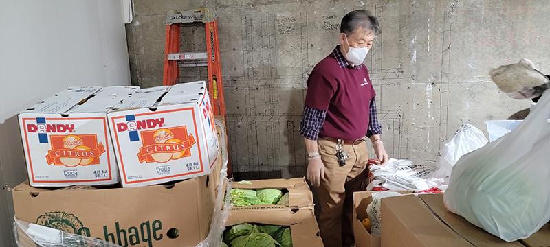 Man in mask standing among boxes of citrus and cabbage
