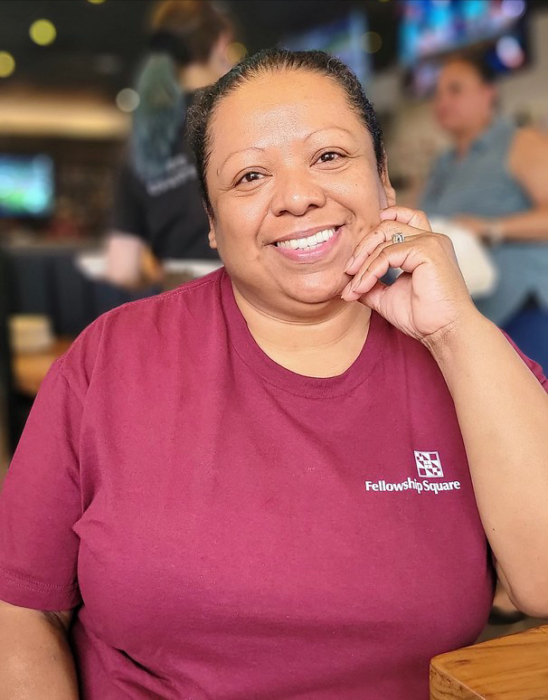 woman leaning on one elbow wearing a red shirt with fellowship square logo on front
