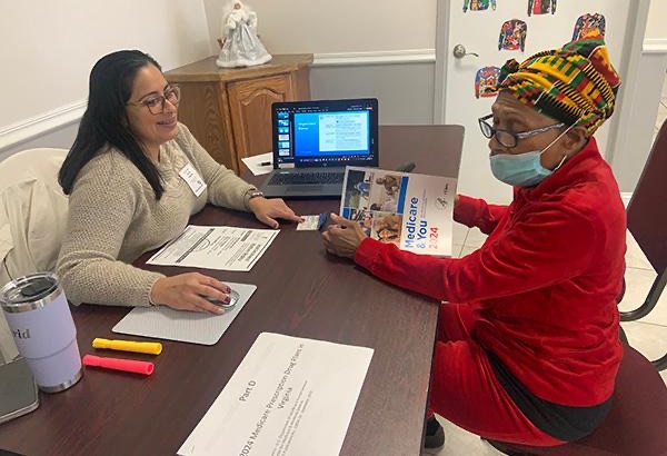 two women seated across from each other at a desk reviewing a 2024 medicare book