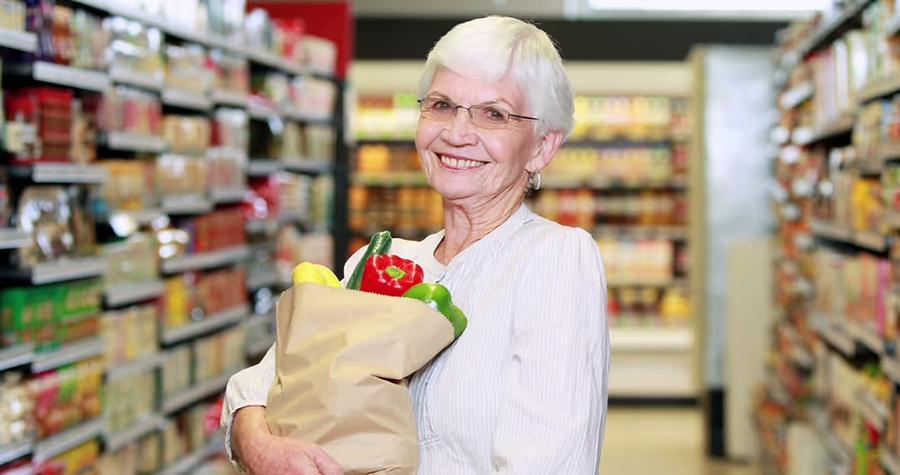 grey haired woman holding a bag of groceries while standing in a grocery store