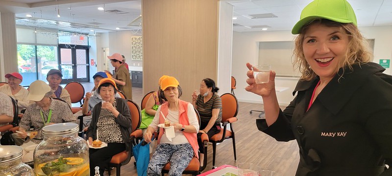 woman in hat holding a drink with seated residents are in background
