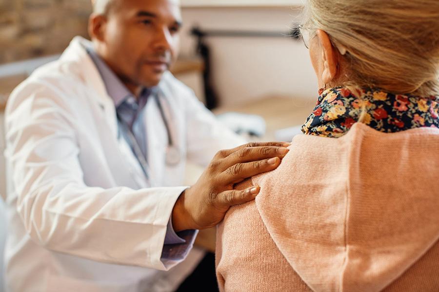 man in white doctor coat with hand placed on woman's shoulder in sign of comfort