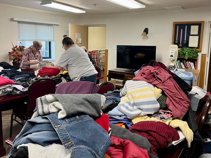 two people sorting clothes with piles of clothes in the foreground