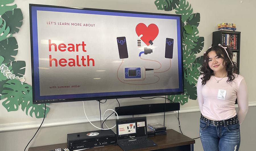 young woman standing in front of a screen displaying a presentation on heart health