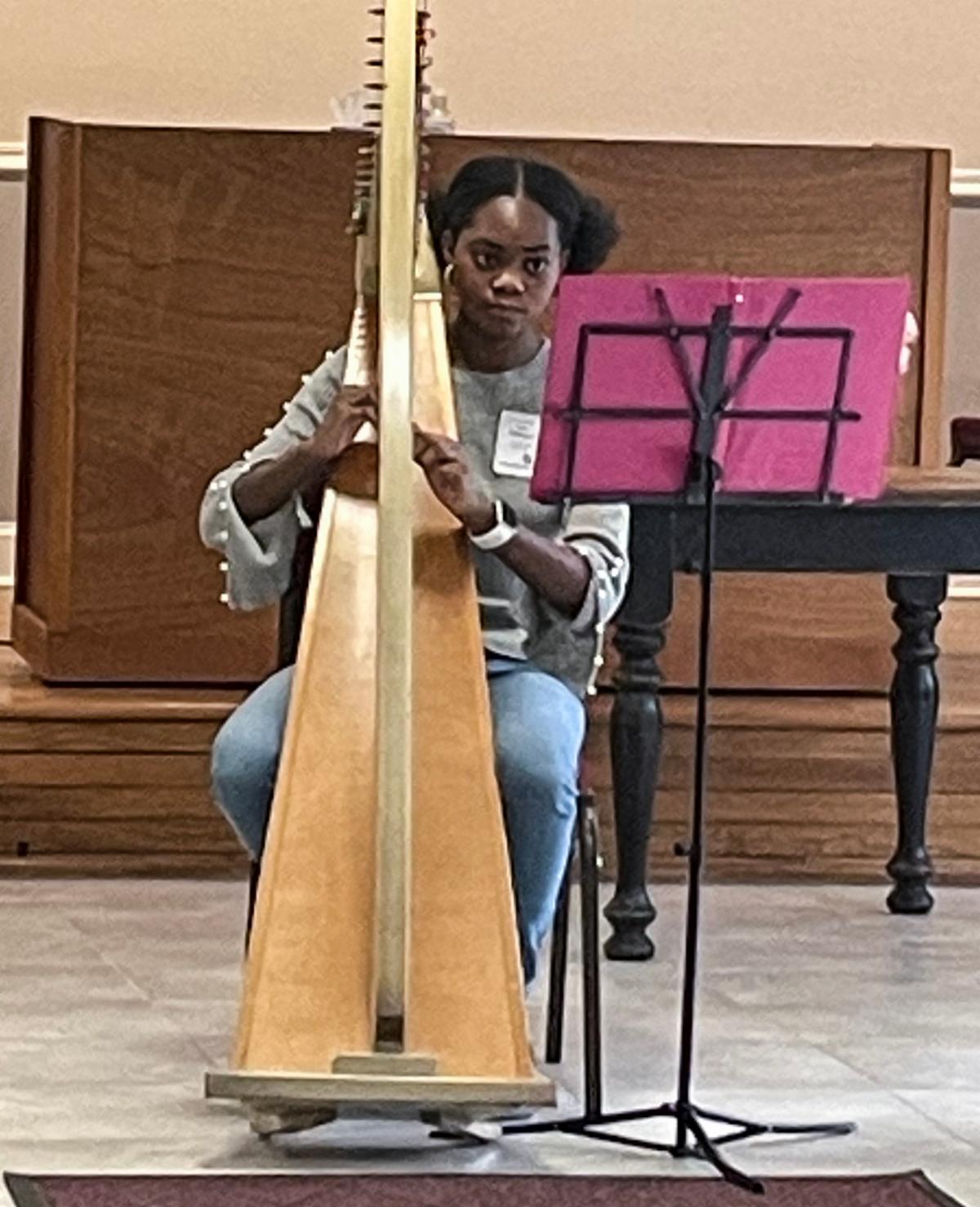 young woman playing a large gold harp