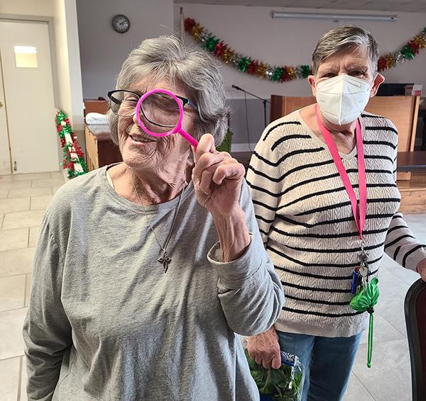 two women one holding a magnifying glass to her eye the other watching her
