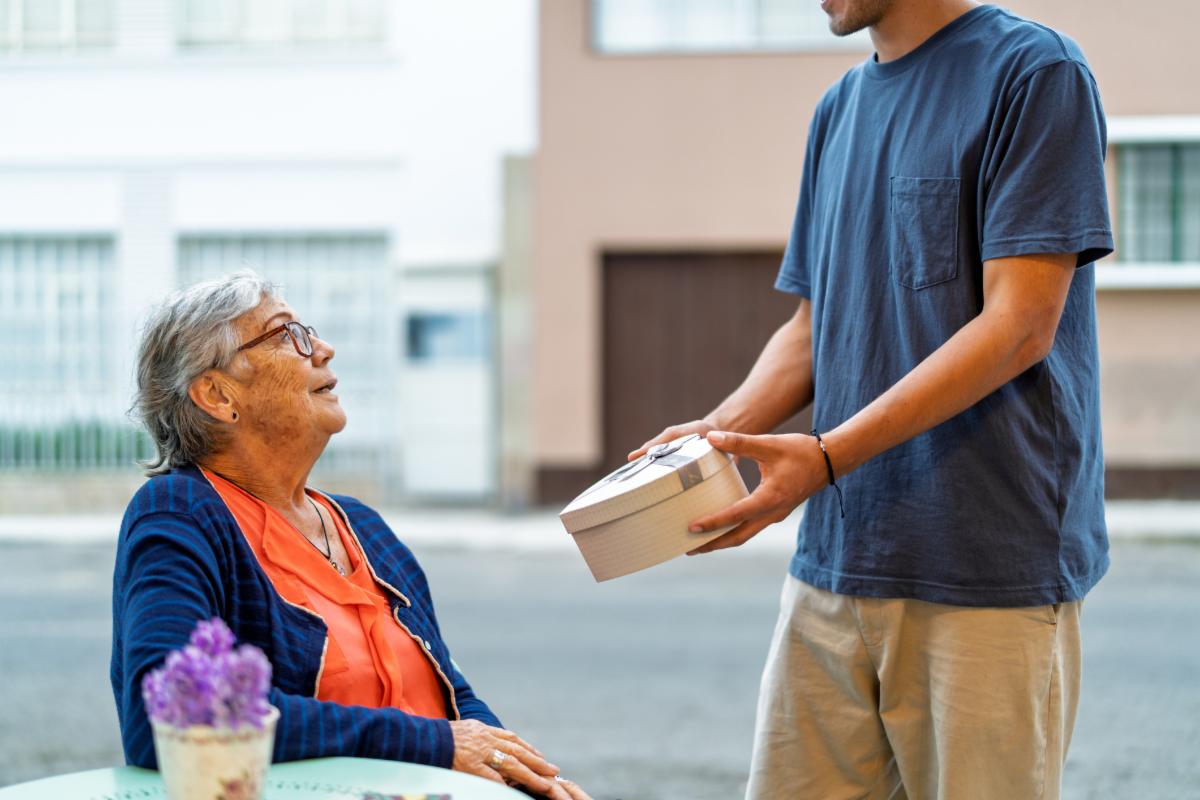Young man sharing a heartfelt moment with his grandmother while giving her a thoughtful gift during a delightful lunch at an outdoor cafe