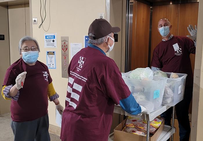 3 volunteers in matching t-shirts load a cart of items onto an elevator