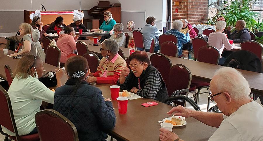 Residents seated at long tables eating birthday cake