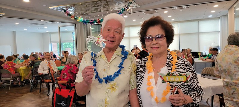 A party Scene Man and woman wearing leis with other residents seated at tables behind them 
