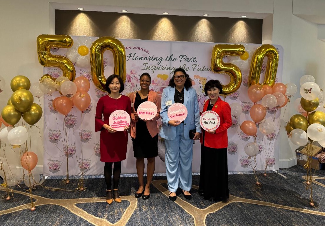 four women holding signs standing in front of a banner and balloons