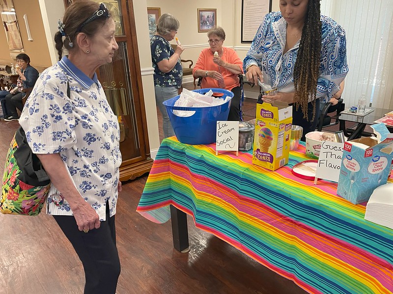 woman stands in front of a table with a rainbow cloth gets and ice cream from woman standing behind
