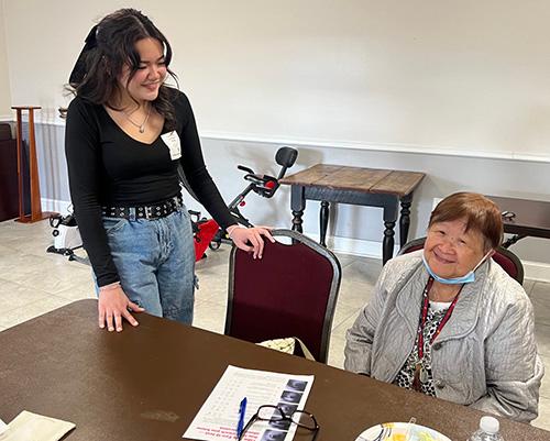 young woman standing next to a seated older woman