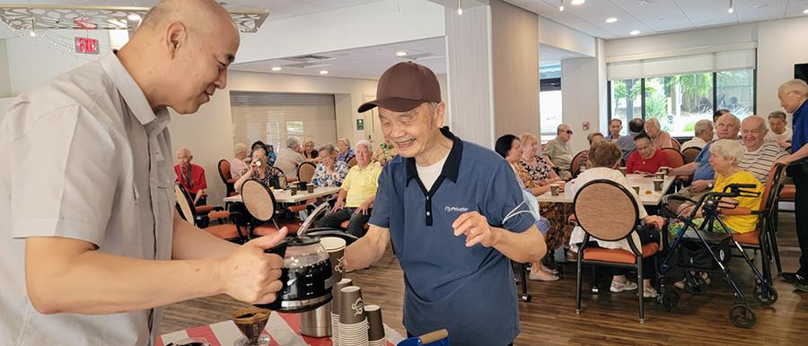 man pouring coffee for another man with people seated at tables in the background