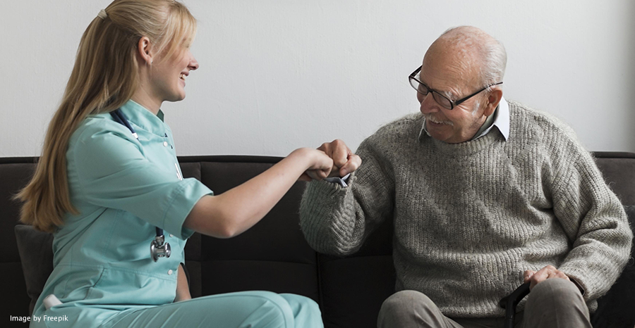 caregiver and older man sitting on a couch together and sharing a fist bump
