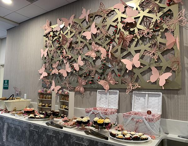 buffet table of cupcakes and treats with butterfly wall decoration above