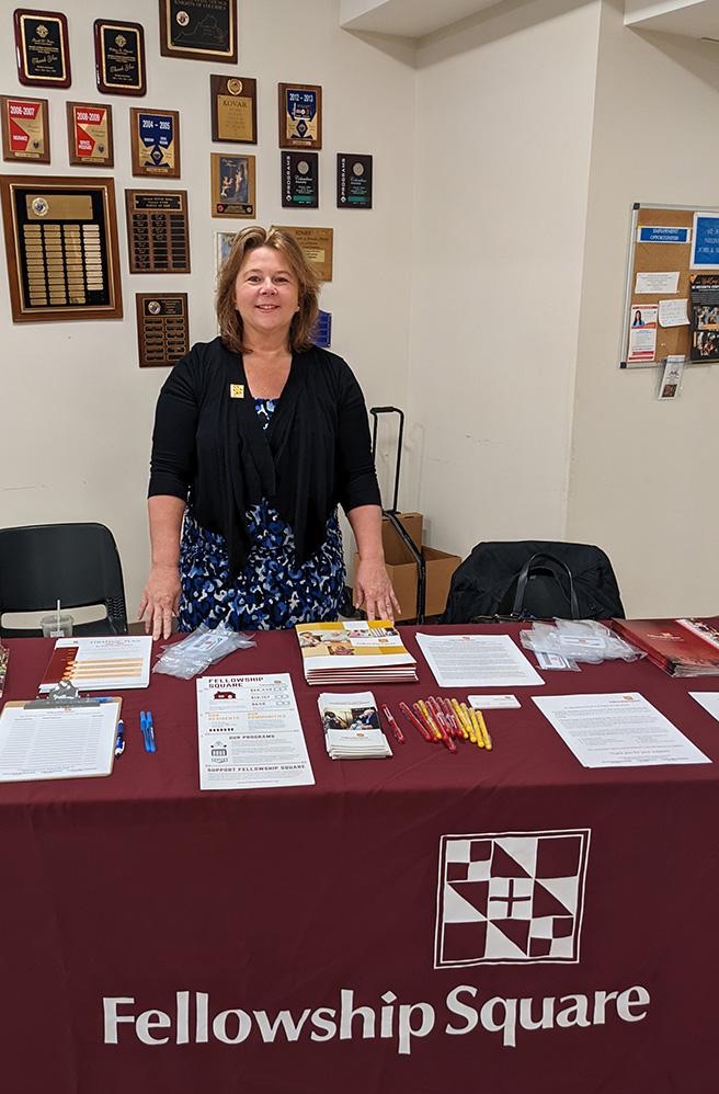 Christy standing behind table with logo and pamphlets on it at event