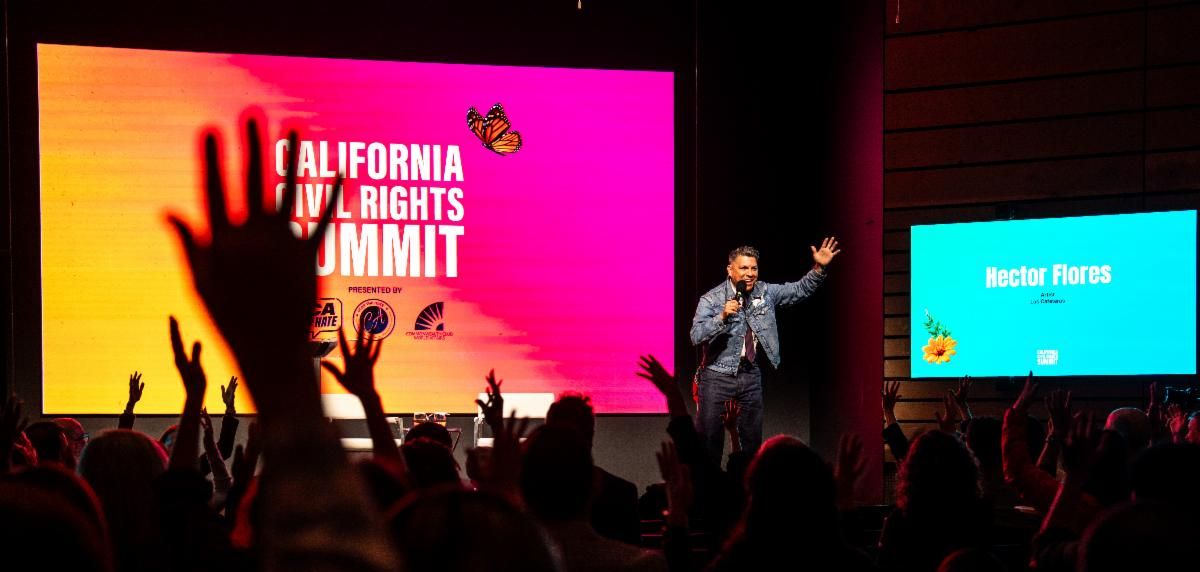 Musician and activist  Hector Flores addresses an engaged audience with raised hands at the California Civil Rights Summit event.