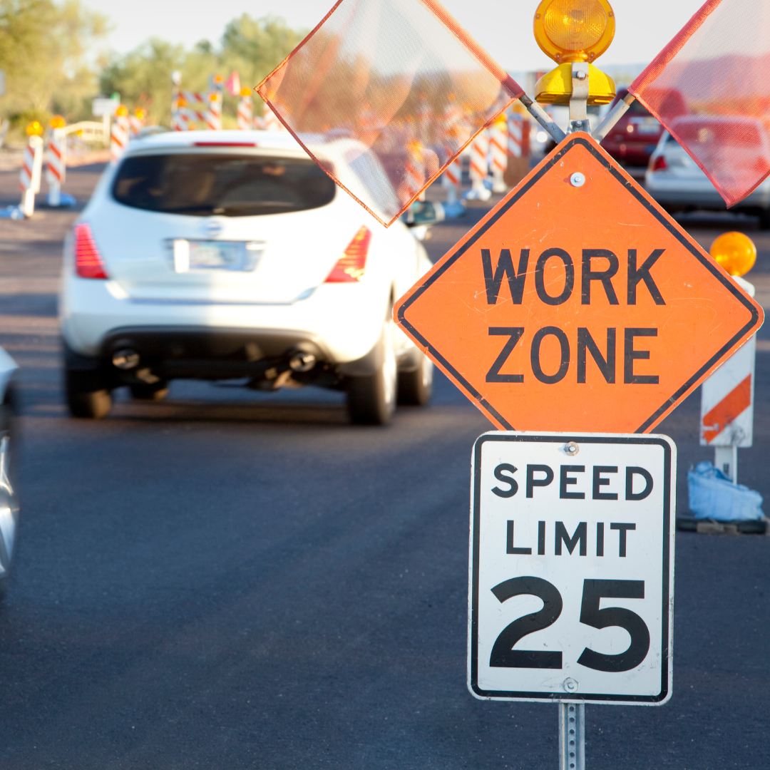 Cars drive past a work zone sign.