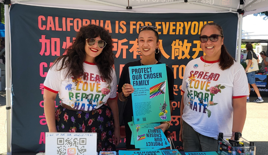 Califronia Civil Rights Department staff smile at a resource table during a Pride event.