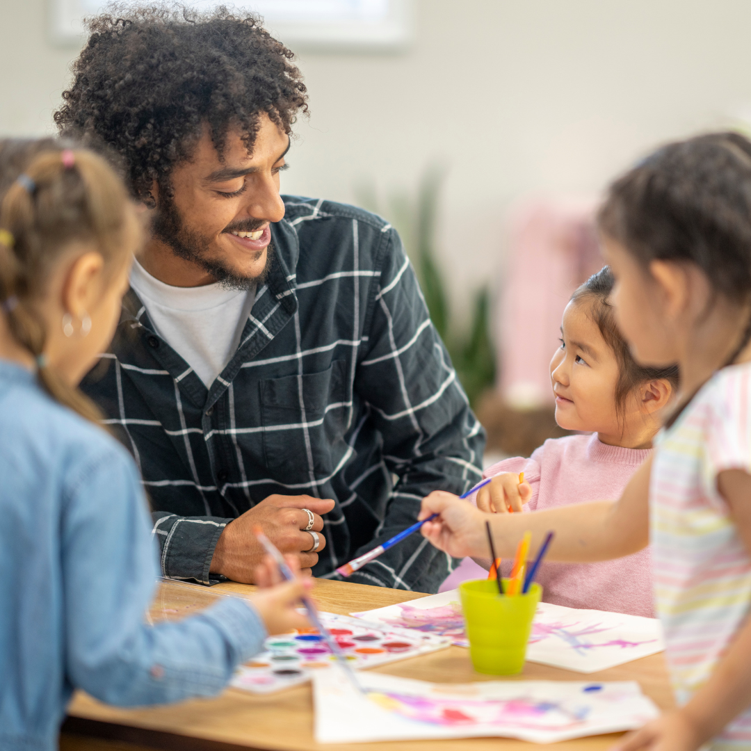 A young man helps children with an art project at a day care.