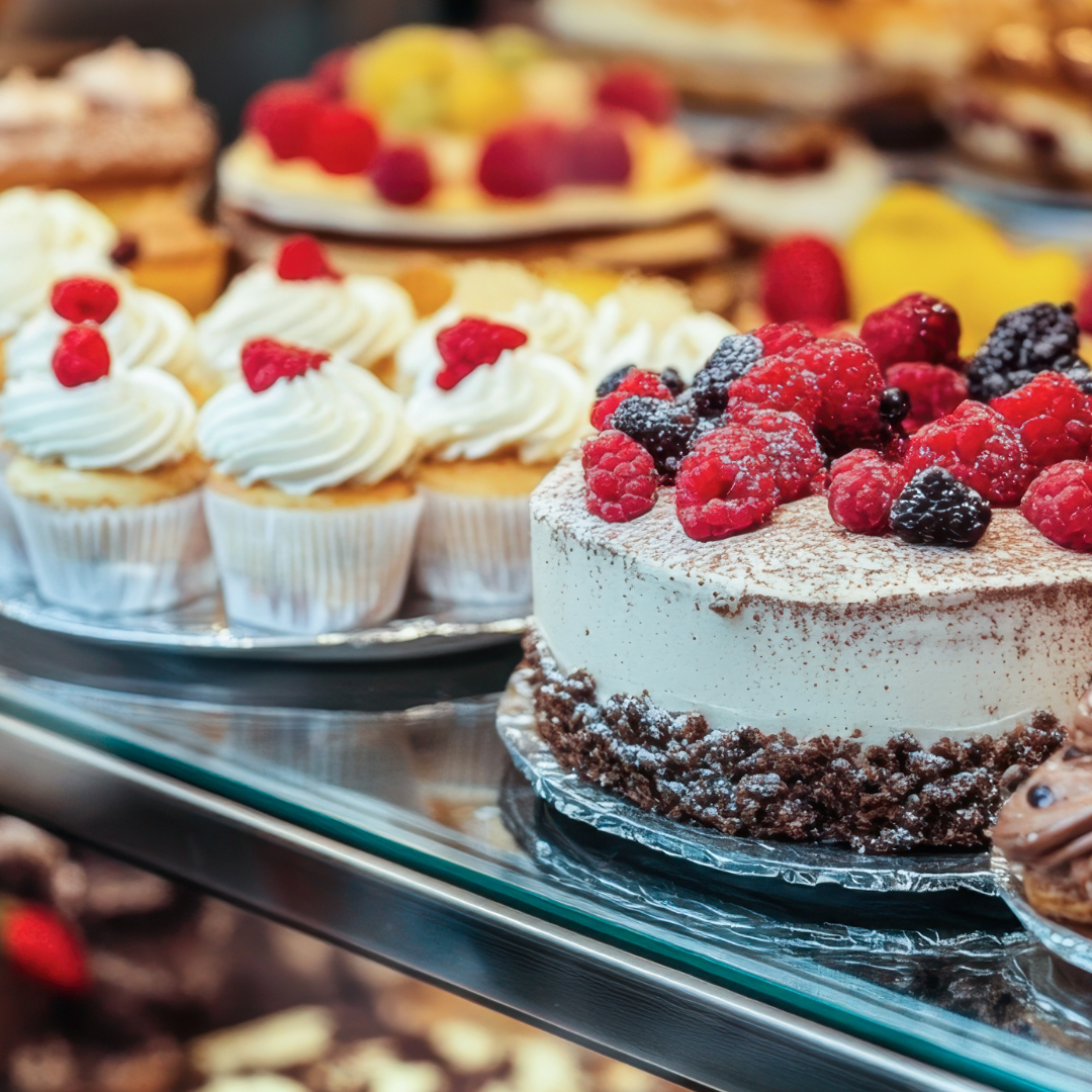 A bakery display shelf with cakes and cupcakes topped with fresh berries.