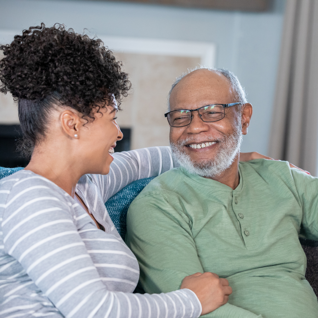 A caregiver puts their arm around their family member and smiles.