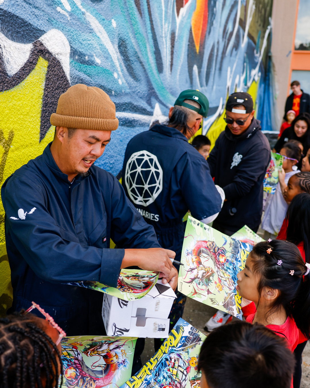 Artists from Illuminaries sign printed copies of their new mural in Oakland for local school children.