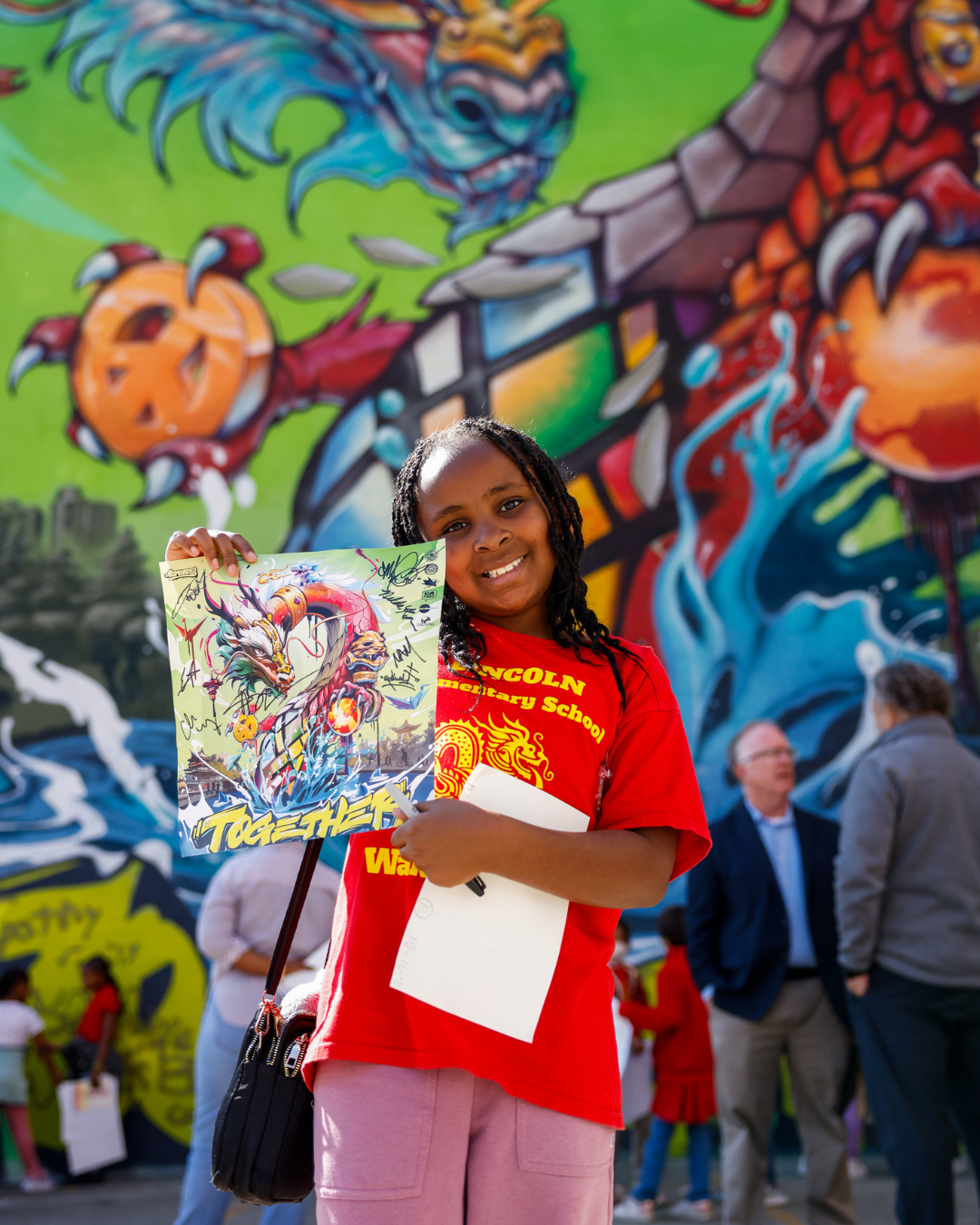 An Oakland third grader smiles with a printed copy of the new Together We Rise mural in Oakland